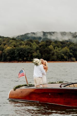 A wooden boat with an American flag floats on a lake against misty mountains and forested shoreline.