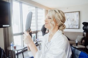 A person in a white robe holds up a hairbrush while getting ready in a bright hotel room.