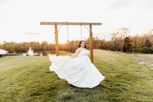 A flowing white wedding dress twirls gracefully across a sunlit grassy field at golden hour.