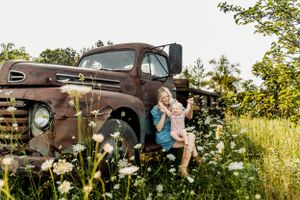 A rustic vintage brown Ford pickup truck sits in a wildflower meadow at sunset during a summer evening.