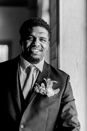 A series of black and white portraits showing a groom in a dark suit with boutonniere smiling near a window.