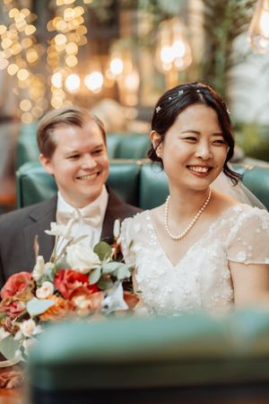 Newlyweds share a joyful moment at their reception with warm bokeh lights and floral bouquet in an elegant venue.