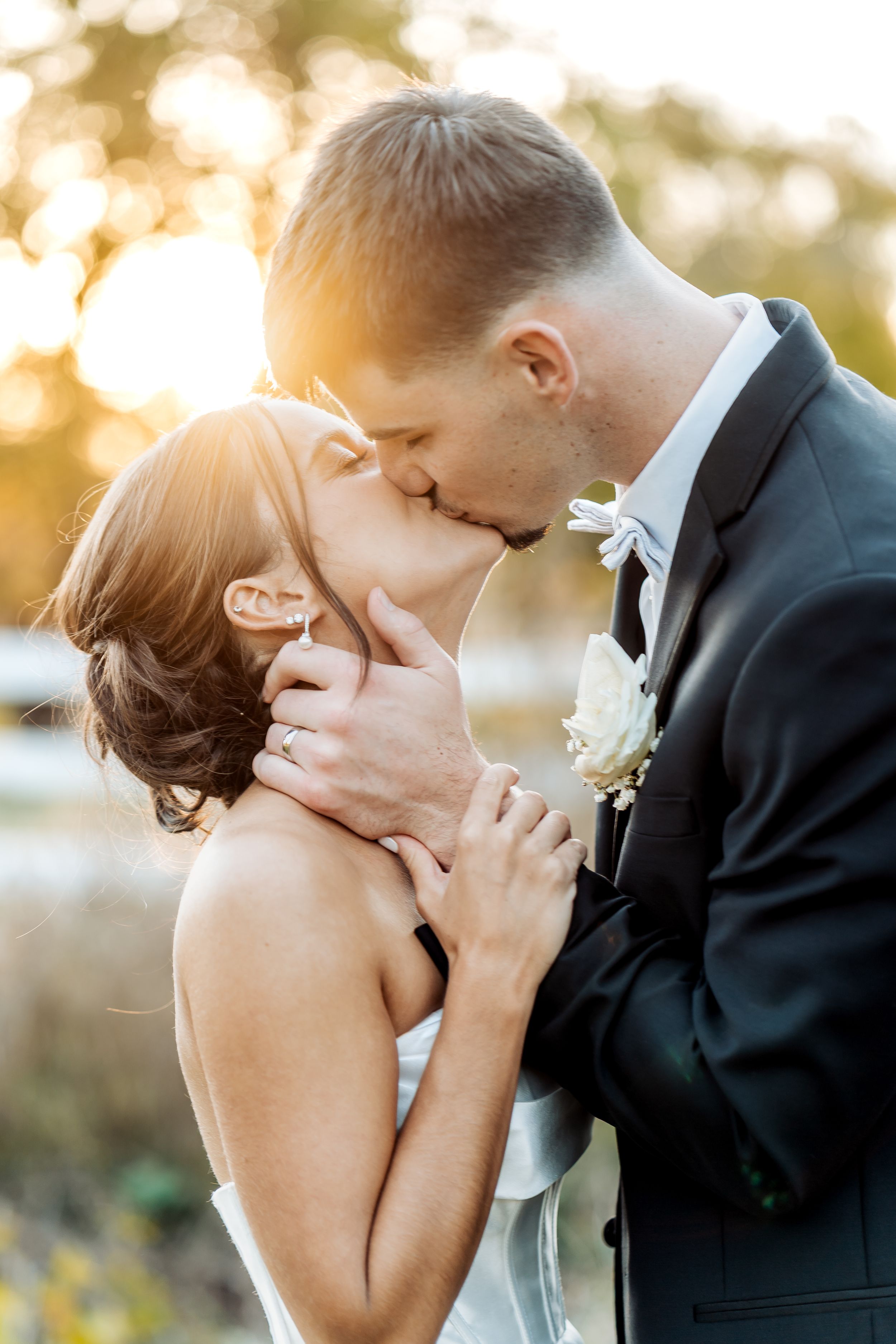 Romantic wedding couple sharing intimate kisses in golden sunlight during outdoor photo session.