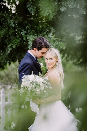 Romantic wedding couple embraces in a lush garden setting with soft green foliage creating a dreamy atmosphere.