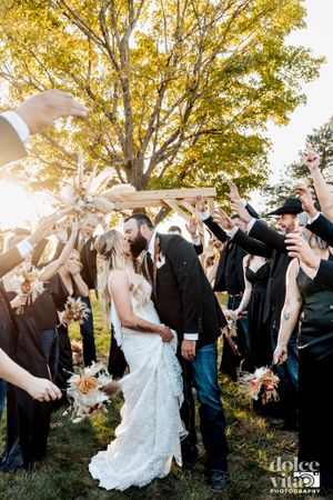 Guests shower the happy couple with flower petals during a joyful autumn wedding celebration under a golden tree.
