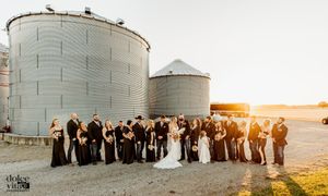 Wedding party poses outdoors against grain silos at sunset, with golden light illuminating the countryside.