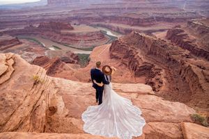 A wedding couple stands on the edge of Dead Horse Point State Park overlooking the dramatic red rock canyons of Utah.