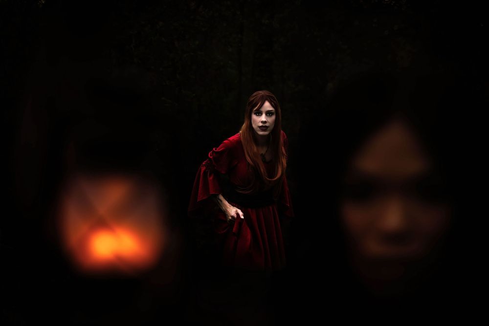 In the foreground in a blurry woman holding up a lantern. In focus in the background is a beautiful vampire huntress that is ready to pounce