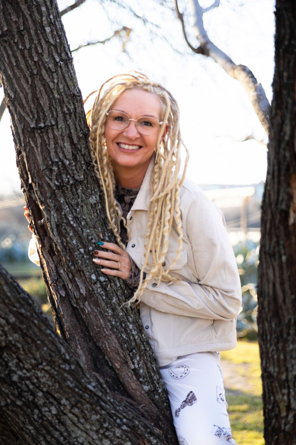 A woman with bright blonde dreads poses on a tree.
