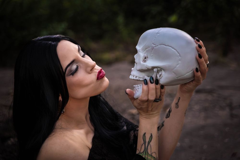 A woman with black hair makes kissy faces at a skull that she is holding up.