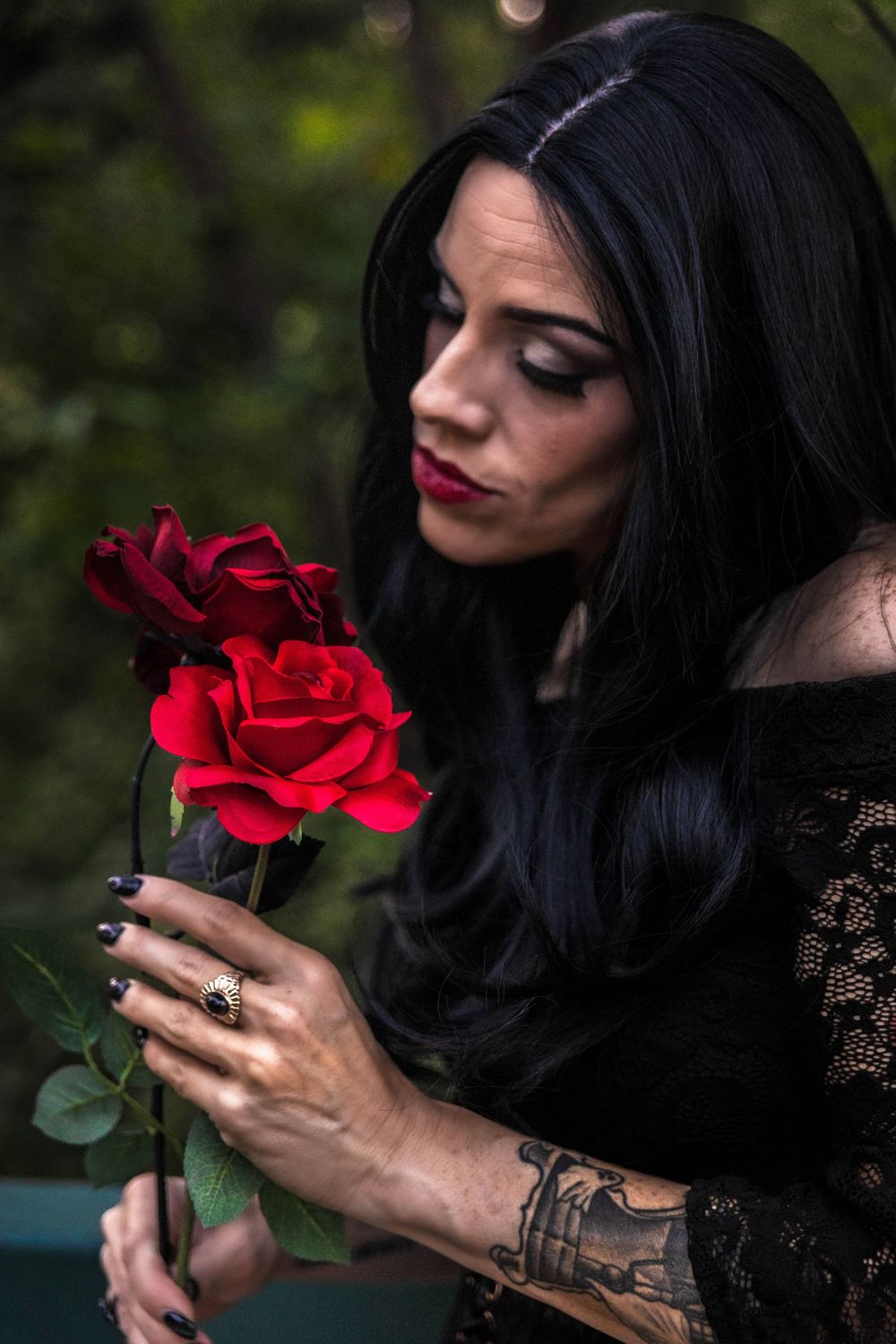A woman with black hair admires a red rose.