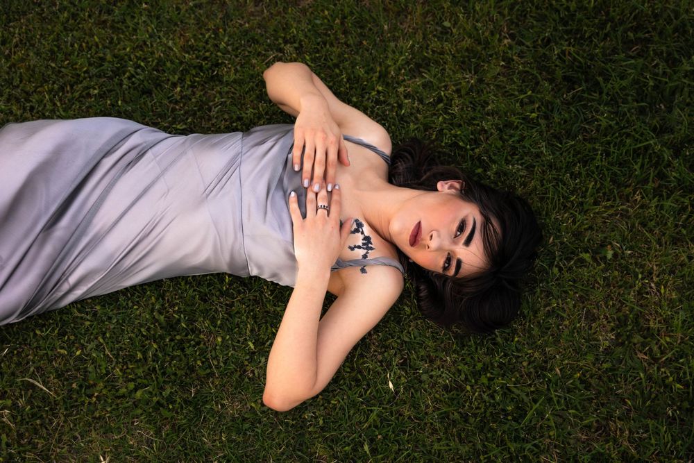 A woman lays in the grass wearing a silver dress.