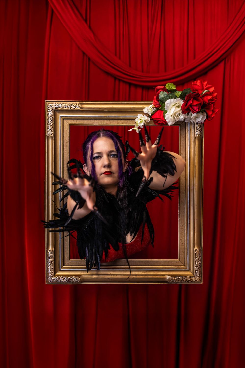 Woman in a red dress and black long nails on a Valentine's Day studio set.