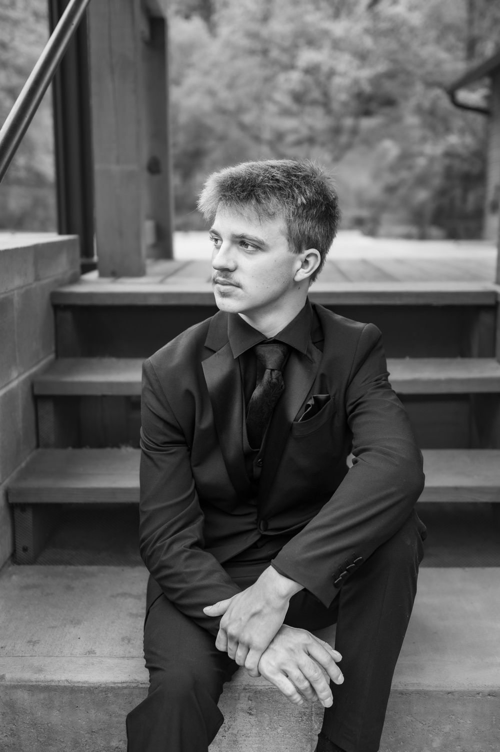 Black and white portrait of a person in formal wear sitting on outdoor steps.