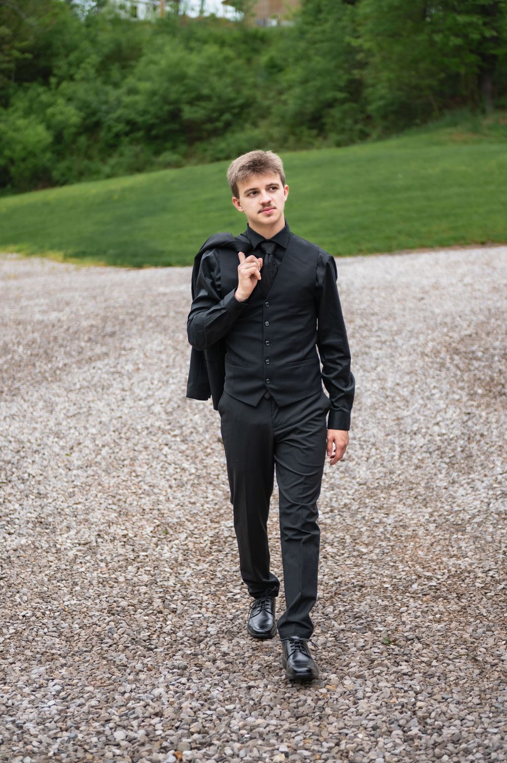 A person walks on a gravel path wearing all black formal attire.