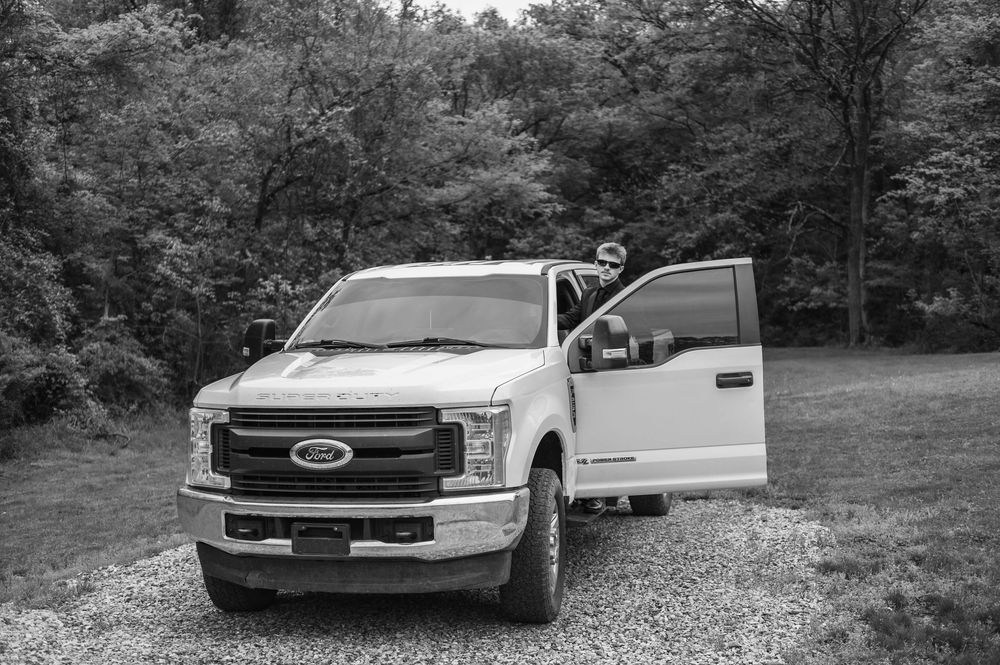 White Ford F-series pickup truck parked on gravel with forest background.