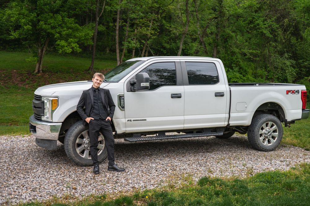 Brand new white Ford Super Duty pickup truck parked on gravel path with lush green forest backdrop.