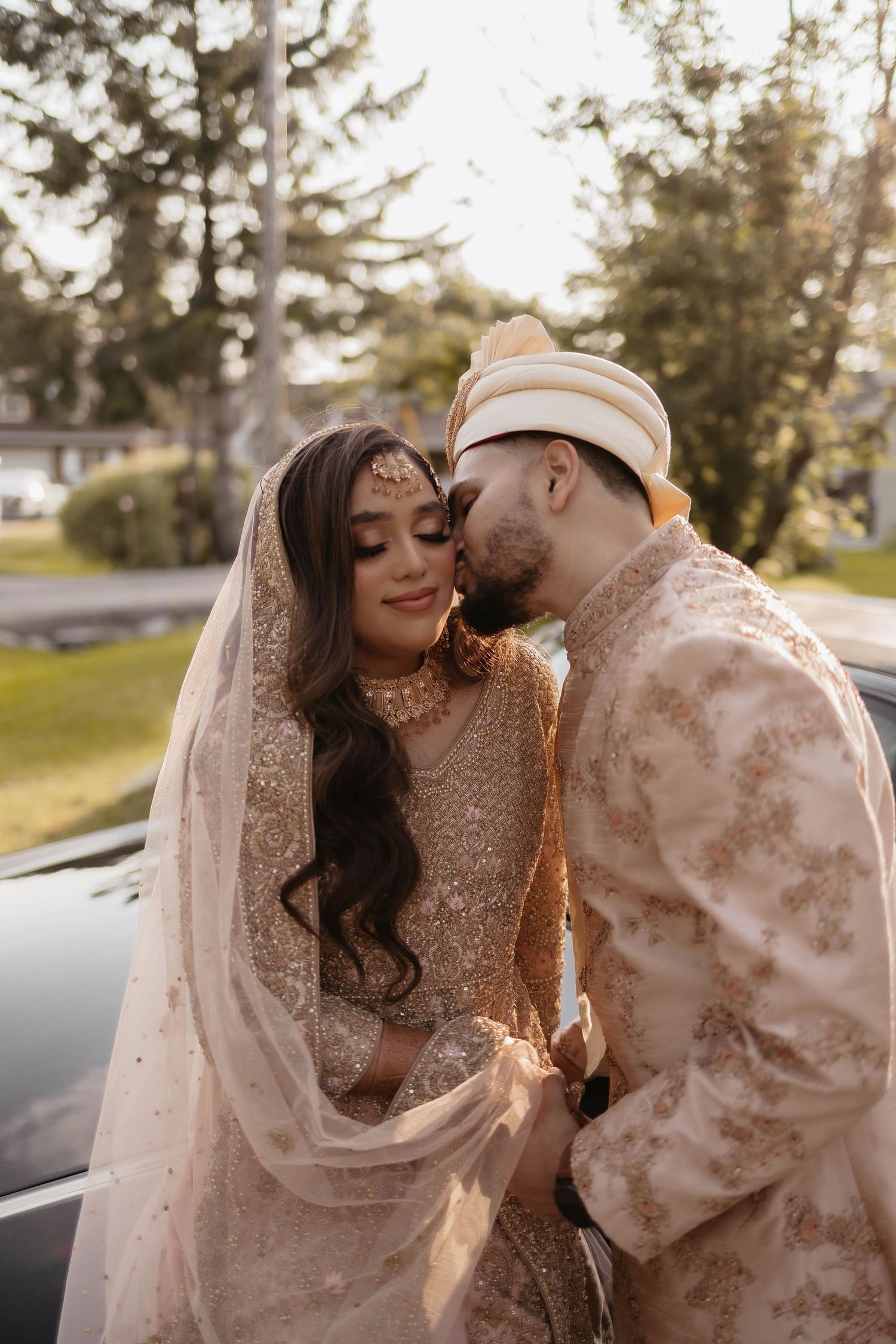 Couple in traditional South Asian wedding attire sharing a tender moment outdoors at golden hour.