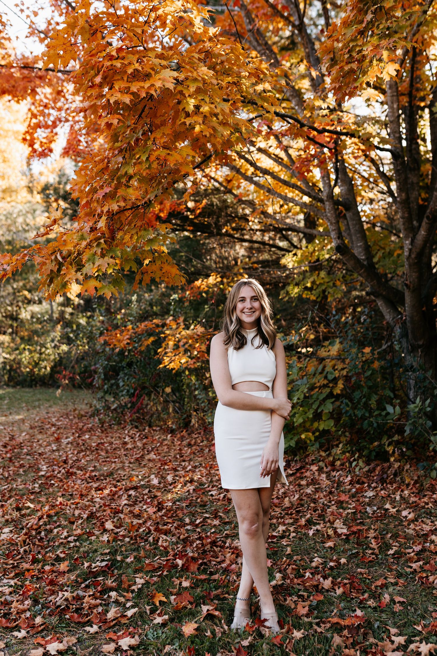 A portrait in a white dress against vibrant autumn trees with orange and red leaves.