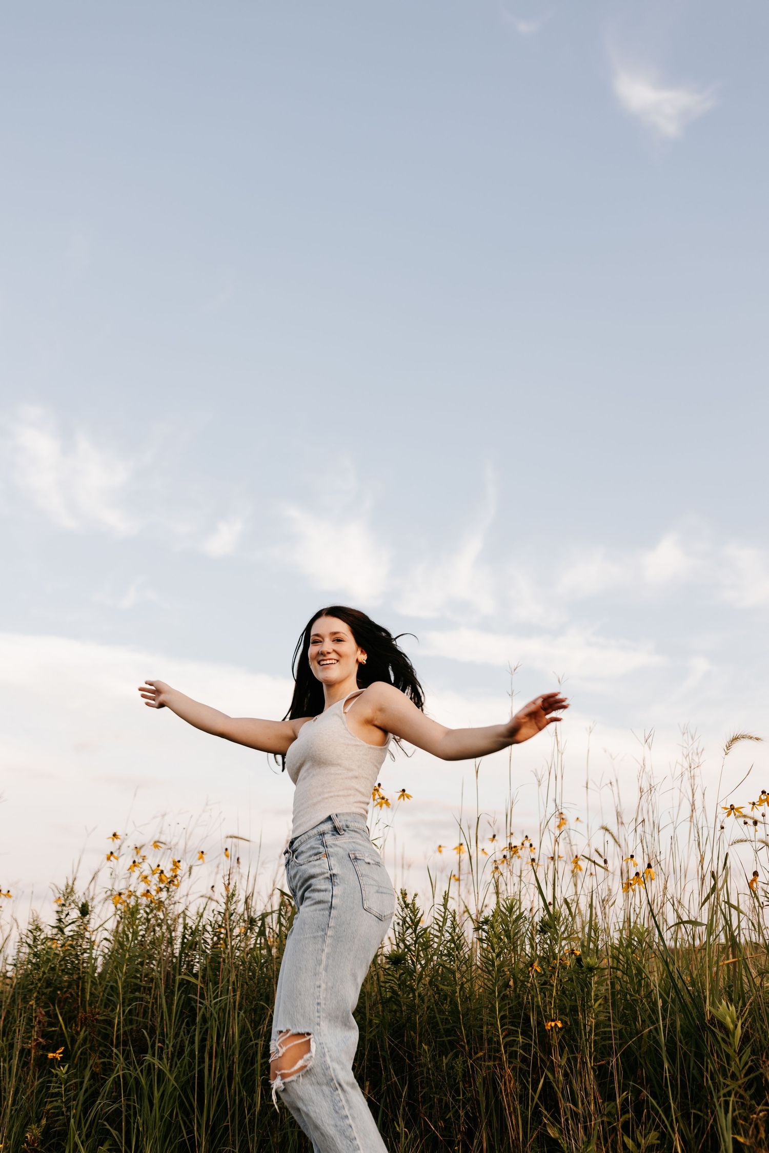 A joyful pose with arms spread wide against a bright sky in a wildflower field.