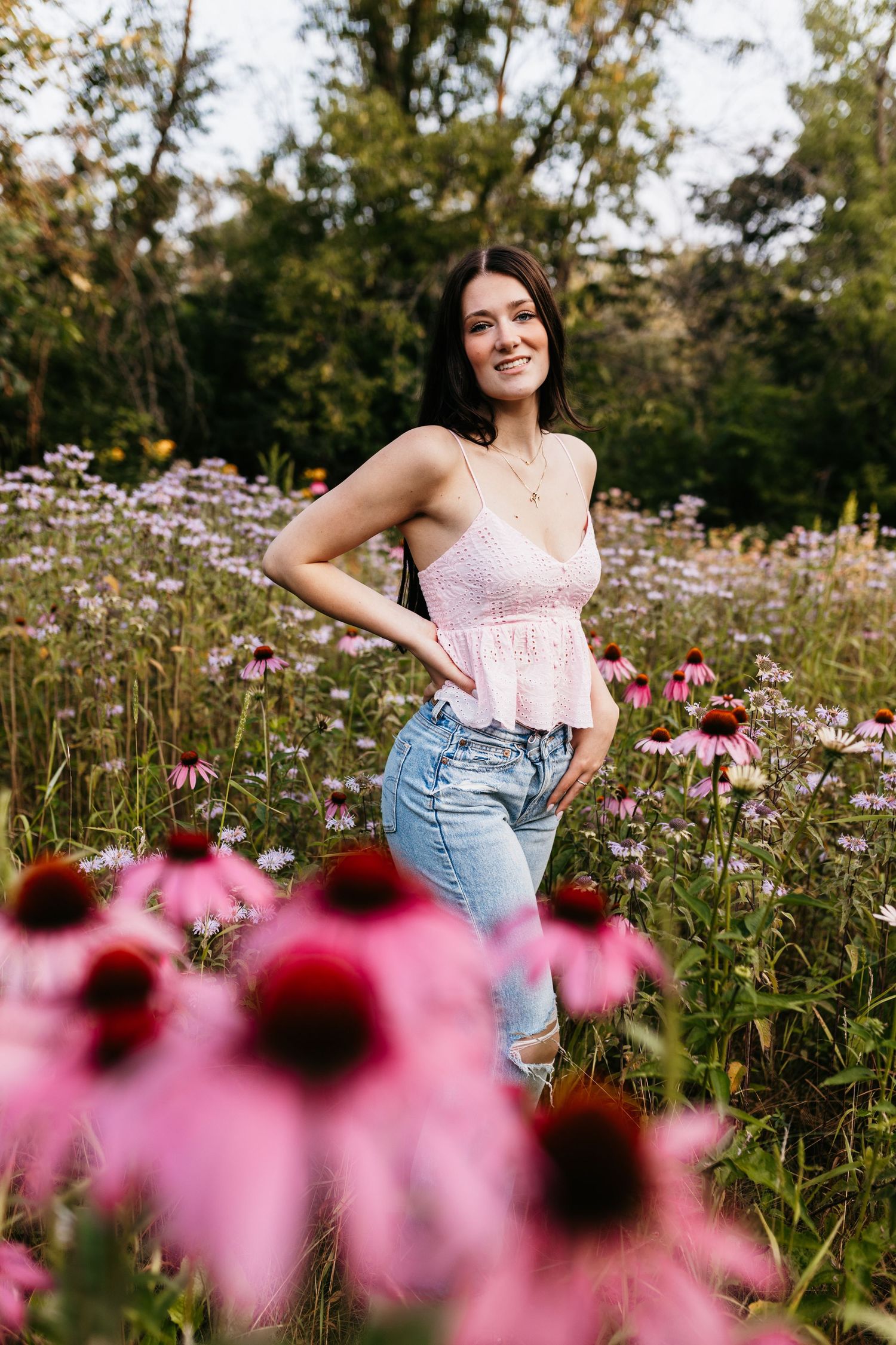 A summer portrait among blooming pink coneflowers wearing a pink top and jeans.