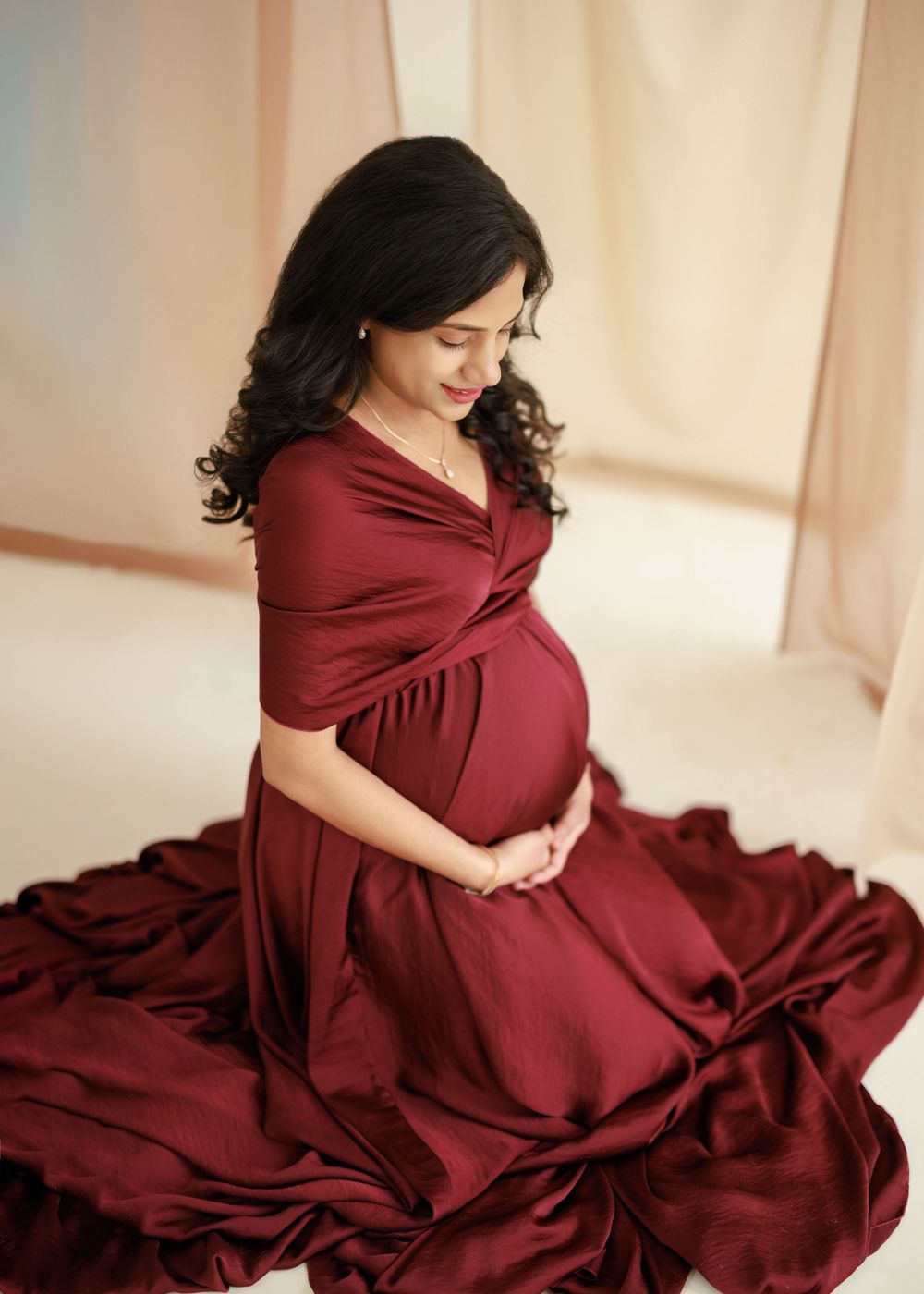 A pregnant woman in a flowing burgundy dress twirls gracefully in a series of connected photos.