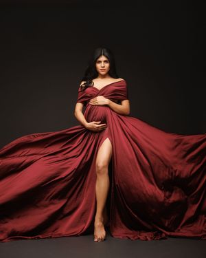 Dramatic maternity photo featuring flowing burgundy gown with thigh-high slit against dark background.
