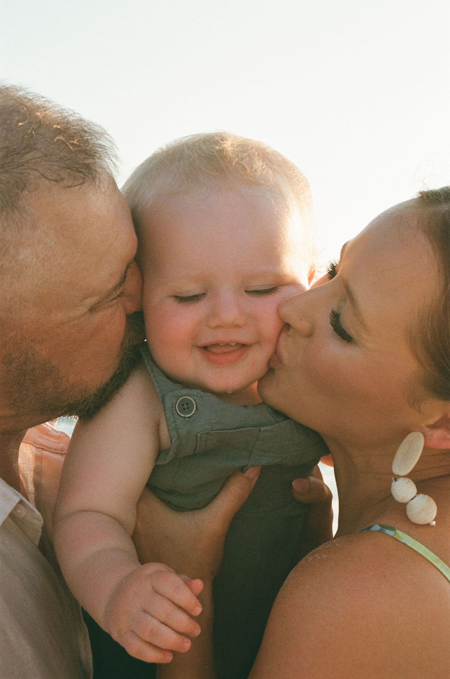 Close-up of baby receiving kisses in warm sunlight.
