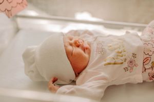 A newborn baby's tiny hand reaching up while wearing a soft white outfit with delicate embroidery.