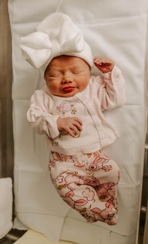 A sleeping newborn wearing a white bow hat and bunny-print outfit stretches peacefully.