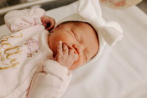 A peaceful newborn baby sleeps soundly in white clothing with delicate embroidered details.