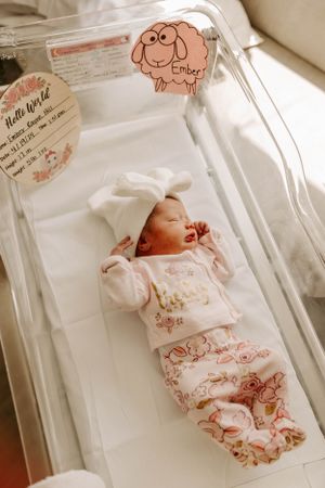 A newborn rests in a hospital bassinet wearing bunny-print pajamas and white bow hat.