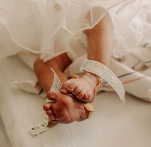 A tiny newborn's feet peek out from beneath a flowing white christening gown.
