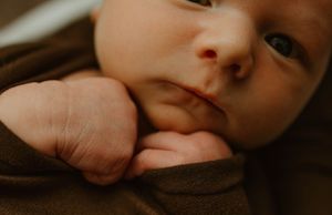 Close-up portrait of baby wrapped in brown fabric with soft, warm lighting.