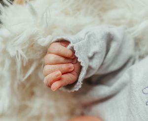 Close-up of tiny newborn baby's hand with lace sleeve detail.