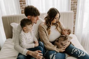 Family lounges together on beige couch near brick wall and white curtains.
