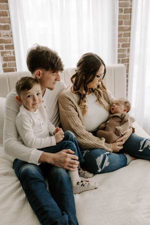 Family relaxing together on white couch against brick wall in casual attire.