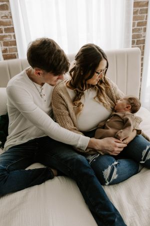 Intimate family moment with parents and baby sitting together on white sofa.
