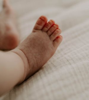 Tiny newborn baby foot against white textile background.