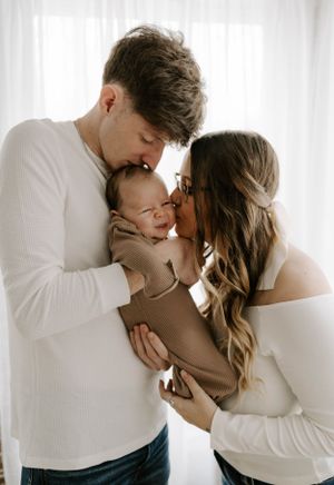 Intimate family portrait with newborn between parents against white backdrop.