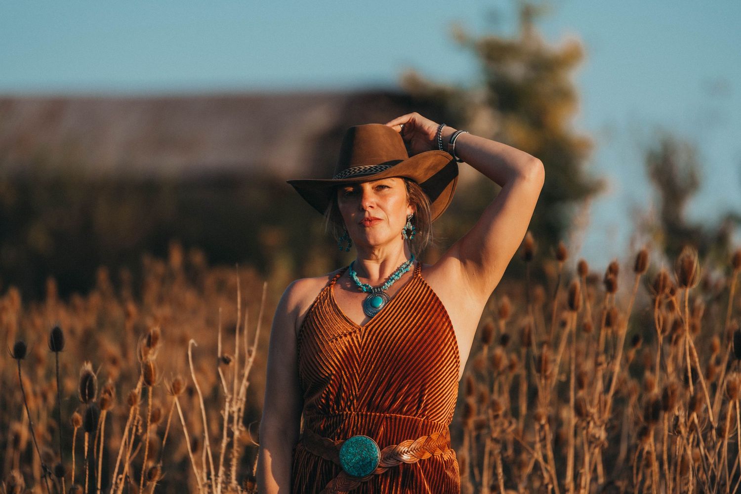 Portrait in golden field wearing western-style outfit with turquoise jewelry at sunset.