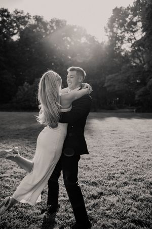 Black and white photo of a joyful couple embracing and dancing in a sunlit outdoor park setting.