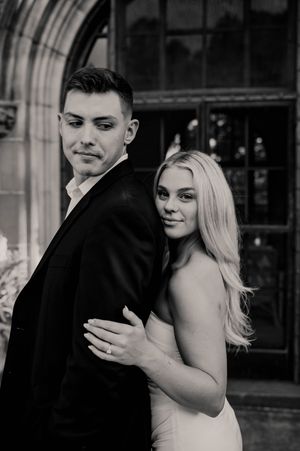 Elegant black and white portrait of a couple in formal wear posing in front of an arched stone building.