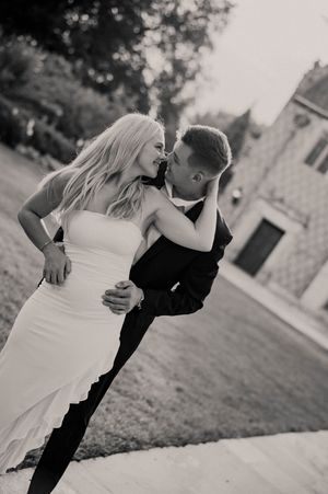 Black and white photo of a couple in wedding attire sharing a romantic dip and kiss outdoors.
