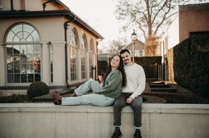 Casual couple sitting on a stone ledge outside a charming brick building at golden hour.