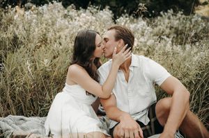 Couple shares a passionate kiss while sitting together in a wildflower meadow during engagement photos.