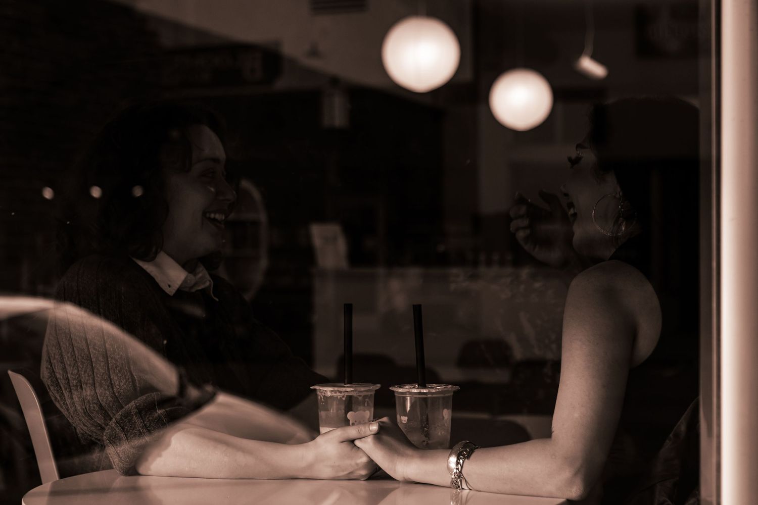 A sapphic couple links hands in an Ashland boba shop. They're photographed in black and white through the window of the shop.