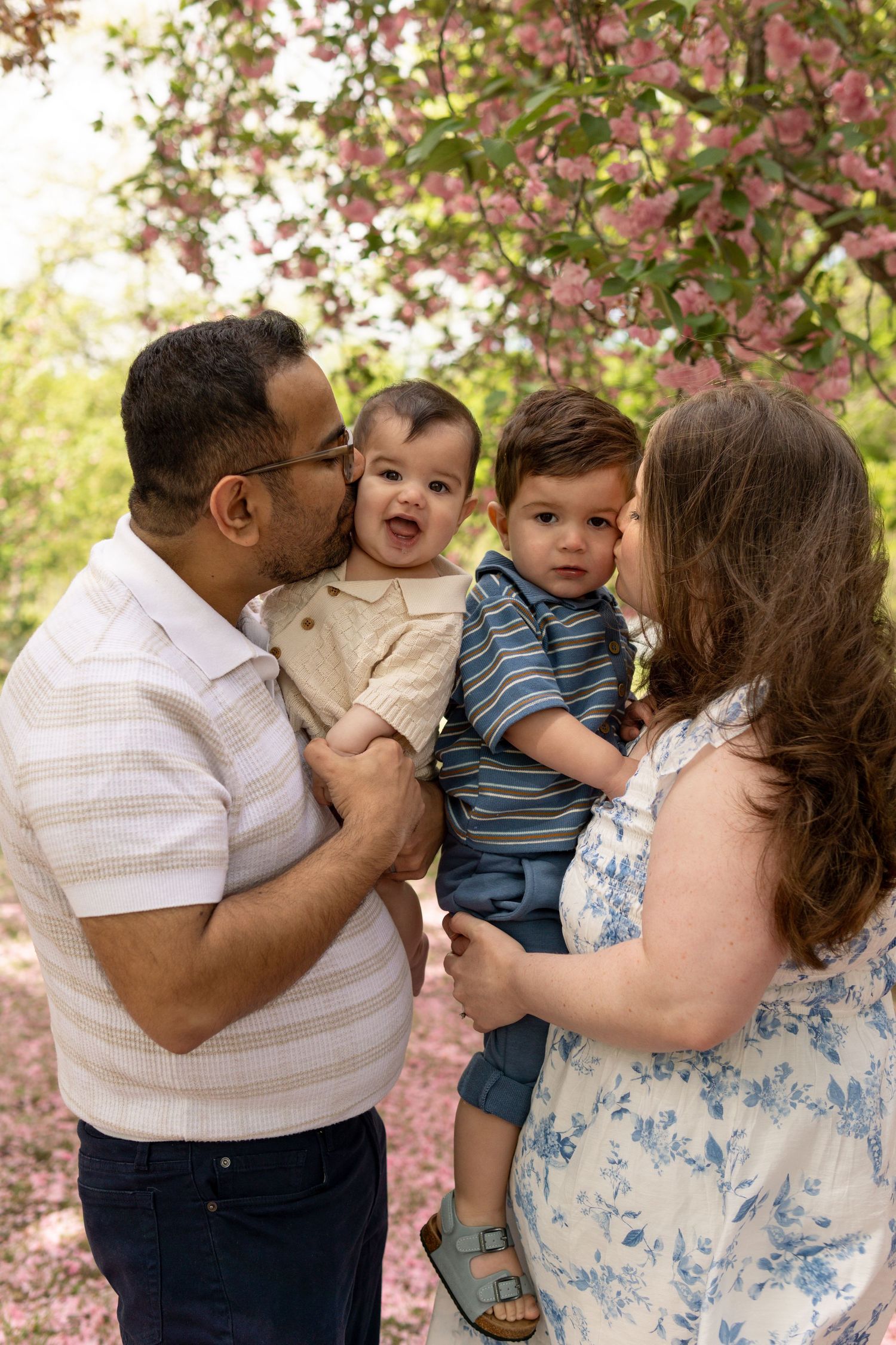 A family shares joyful moments together under blooming pink cherry blossoms in a spring outdoor photo session.