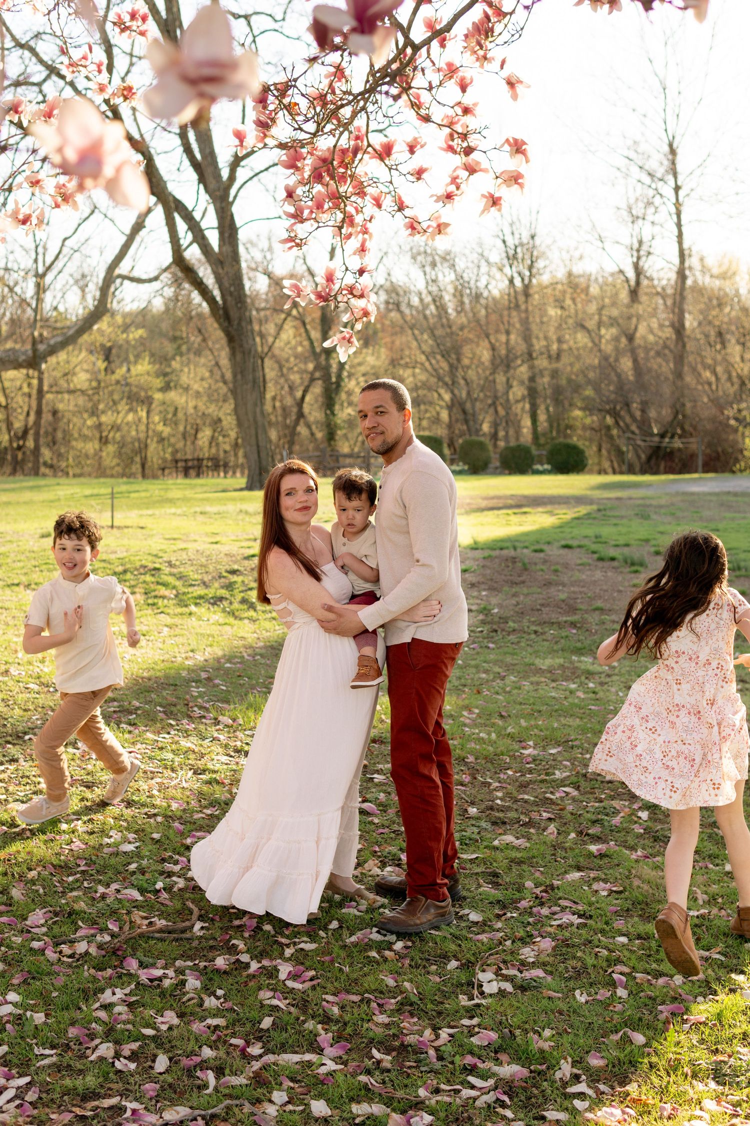 Spring portrait of parents with children running and playing in a flower-filled meadow under blooming pink cherry trees.