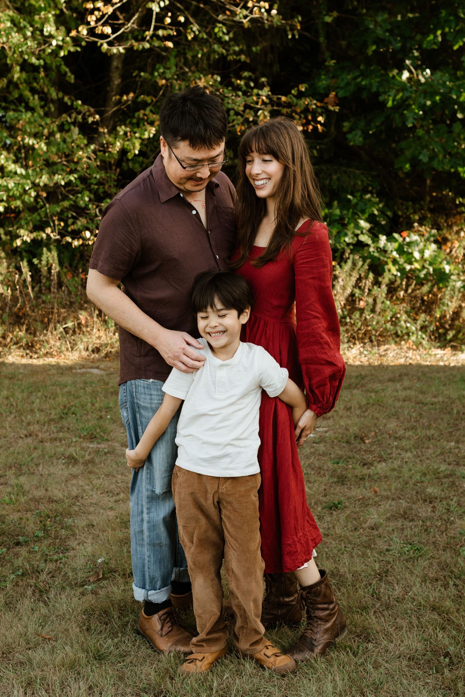 A family stands together outdoors, with autumn foliage in the background.